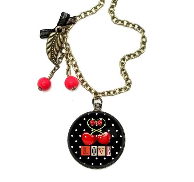 May include: A black and white polka dot necklace with a red cherry charm and the word "LOVE" in red and white letters. The necklace has a gold chain and two red cherry charms hanging from it.