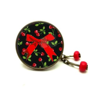 May include: A black and red cherry-themed pendant with a red bow and a chain with red cherry charms.