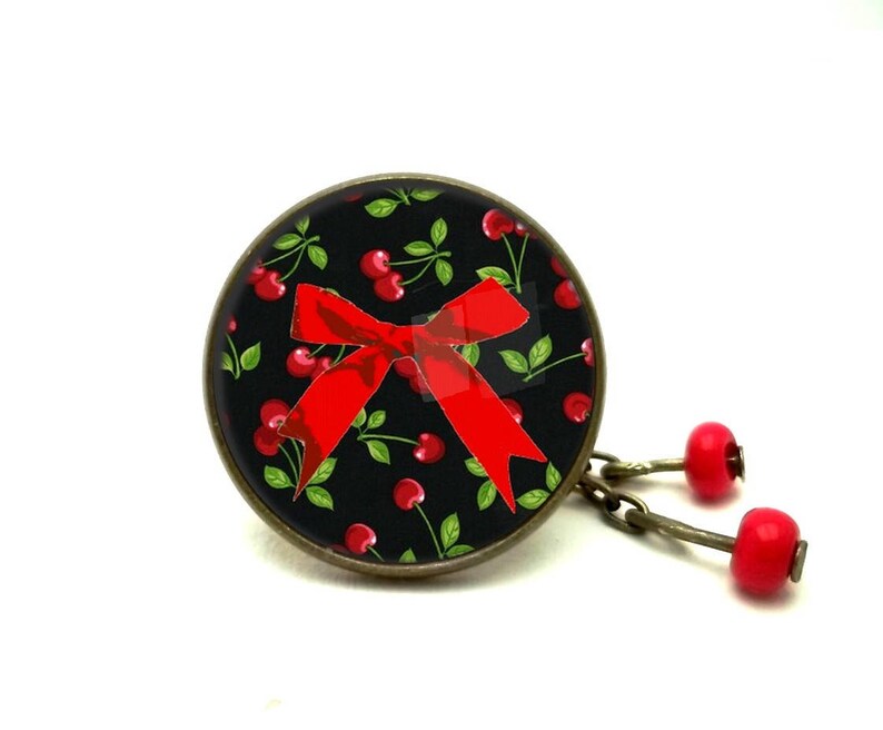 May include: A black and red cherry-themed pendant with a red bow and a chain with red cherry charms.