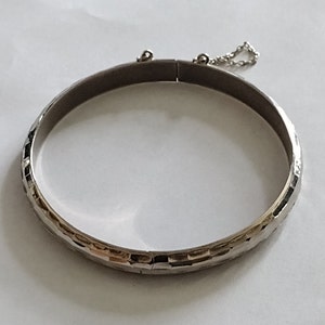 May include: A silver bangle bracelet with a textured design and a small chain attached to the clasp.