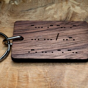 May include: A wooden keyring with a silver ring. The wood is dark brown with a grain pattern. The keyring has the word "Forever" engraved in braille.