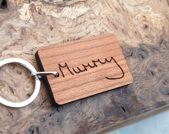 May include: A wooden keychain with a silver key ring. The wood is a light brown color and the keychain has the word "Mummy" engraved on it.
