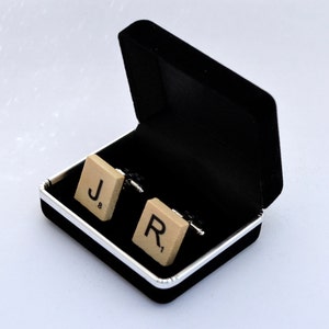 May include: A pair of cufflinks in a black velvet box. The cufflinks are made of wood and have the letters "J" and "R" on them.