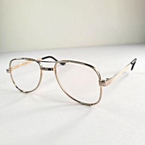 May include: Aviator-style spectacles featuring a thin, polished gold-tone metal frame with a double bridge design. The lenses are clear and transparent, and the temple arms are finished with black plastic tips at the ends for a secure fit.