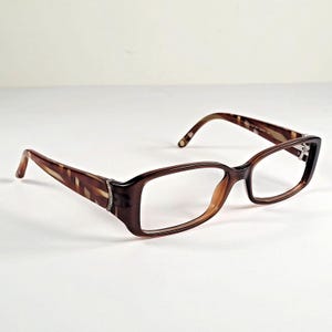 May include: Rectangular spectacles featuring a dark brown tortoiseshell pattern on the frames and temples. The temples include a silver-toned metallic accent near the hinges, and the overall design has a glossy finish with clear lenses.