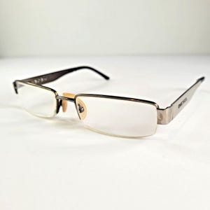 May include: A pair of Diesel eyeglasses with a rectangular, half-rim design. The frames are a combination of silver and black, with the brand name "DIESEL" printed on the temple. The lenses are clear, and the nose pads are a light beige color.