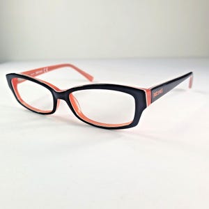 May include: Black and coral-colored rectangular eyeglasses. The frames are black on the outside and coral on the inside. The temples are black with the brand name "Just Cavalli" in coral.