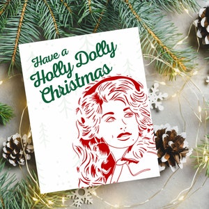 May include: A white card with green text that reads "Have a Holly Dolly Christmas". A red silhouette of Dolly Parton is on the card.