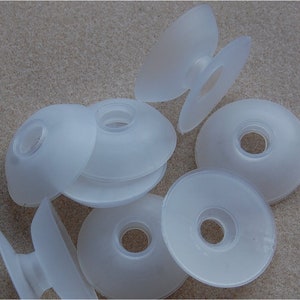 May include: A collection of translucent, circular suction cups made of flexible material. Each suction cup features a concave, bowl-like shape with a central hole and a small, protruding stem on the reverse side, designed for attachment to smooth surfaces.
