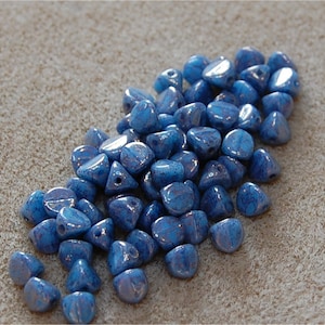May include: A pile of blue iridescent glass beads in a triangular shape. The beads have a speckled, marbled effect.