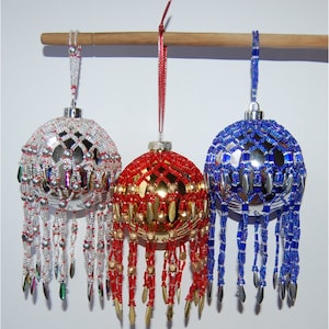 May include: Three beaded Christmas ornaments, one silver with white beads, one gold with red beads, and one silver with blue beads.