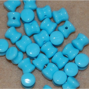 Könnte beinhalten: Eine Sammlung von türkisblauen Glasperlen, einige sind rund und einige sind wie ein doppelseitiger Knopf geformt.