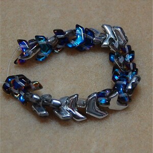 May include: A silver and blue glass bead bracelet with a chevron pattern. The beads are iridescent and have a metallic finish.