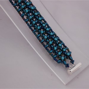 Op de afbeelding: Een tealblauwe kralen armband met een zilveren sluiting. De armband is gemaakt met meerdere strengen kralen in een herhalend patroon.