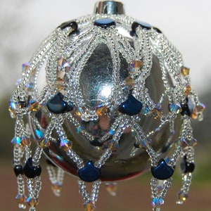 May include: A silver Christmas bauble with a beaded design. The bauble is decorated with blue and iridescent beads.