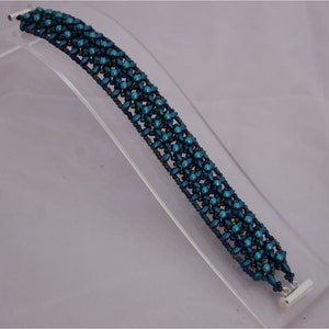 Pode incluir: Um bracelete de contas azul turquesa com um fecho prateado. O bracelete &eacute; feito de pequenas contas redondas que s&atilde;o dispostas em um padr&atilde;o geom&eacute;trico.