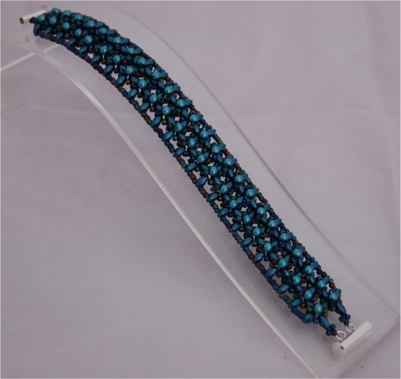 Pode incluir: Um bracelete de contas azul turquesa com um fecho prateado. O bracelete &eacute; feito de pequenas contas redondas que s&atilde;o dispostas em um padr&atilde;o geom&eacute;trico.