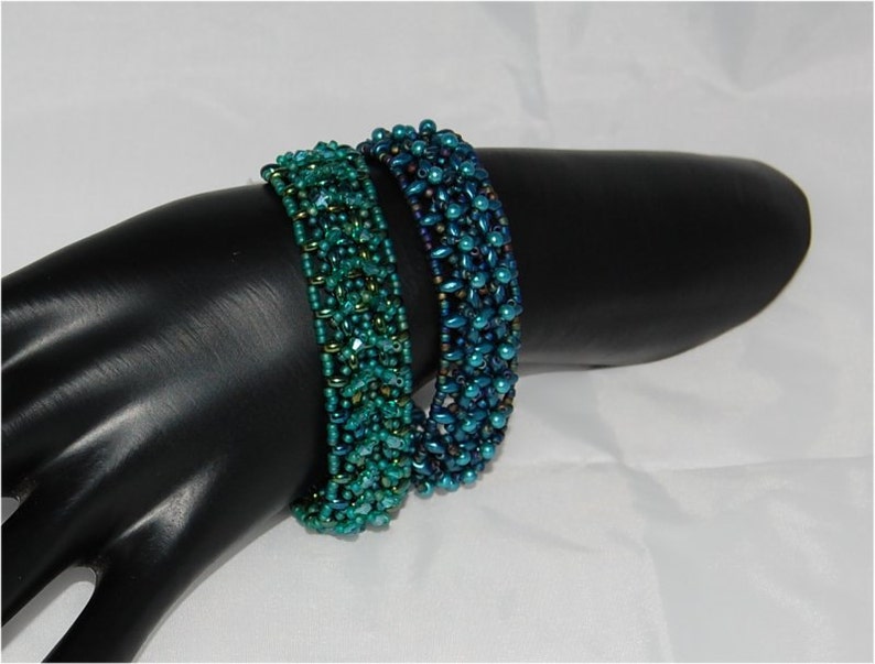 Pode incluir: Duas pulseiras de contas, uma verde e outra azul, em um bra&ccedil;o de manequim preto. As pulseiras s&atilde;o feitas de pequenas contas iridescentes.