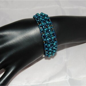 Pode incluir: Um bracelete de contas azul turquesa com um padr&atilde;o tecido. O bracelete &eacute; feito de pequenas contas redondas que s&atilde;o dispostas em um design geom&eacute;trico.