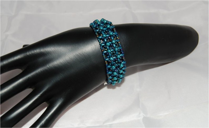 Pode incluir: Um bracelete de contas azul turquesa com um padr&atilde;o tecido. O bracelete &eacute; feito de pequenas contas redondas que s&atilde;o dispostas em um design geom&eacute;trico.