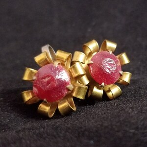 May include: A pair of gold-tone earrings with red glass stones set in a flower design.