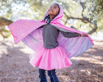 May include: A young person wearing a pink and blue hooded cape with a pink tulle skirt and blue jeans. The cape has a sparkly iridescent finish.