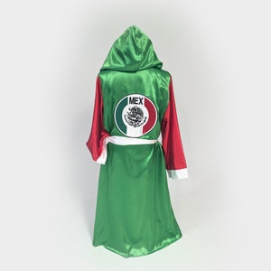 May include: Green and red satin boxing robe with a white hood. The robe has a white sash and a circular patch with the word "MEX" and the Mexican coat of arms.