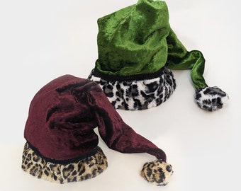 May include: Two velvet elf hats with long tails and leopard print trim. The hats are green and burgundy.