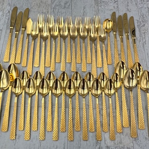 May include: A set of 48 gold-plated flatware, including forks, knives, and spoons. The flatware has a textured, hammered finish.