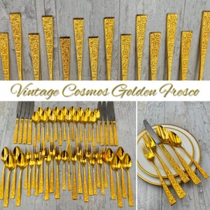 May include: Vintage Cosmos Golden Fresco flatware set in gold. The set includes forks, knives, spoons, and a serving spoon. The flatware has a textured, embossed design.
