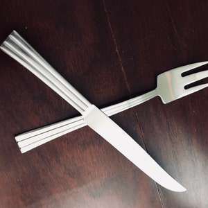 May include: A silver fork and knife crossed on a dark brown wooden surface.
