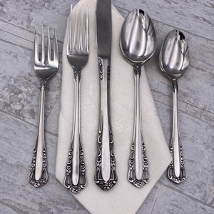 May include: A set of five silver-plated flatware pieces, including a knife, fork, and three spoons, with ornate floral designs on the handles. The flatware is arranged on a white napkin.