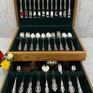 May include: A wooden cutlery chest with a green velvet interior. The chest is open, revealing a set of silver-plated cutlery, including forks, knives, spoons, and serving pieces.