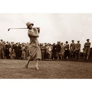 May include: A woman wearing a hat and a skirt swings a golf club as a crowd of spectators looks on.