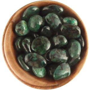 May include: A wooden bowl filled with polished emerald gemstones. The gemstones are a deep green color with dark inclusions, and they have a smooth, rounded shape. The bowl is made of light-colored wood.