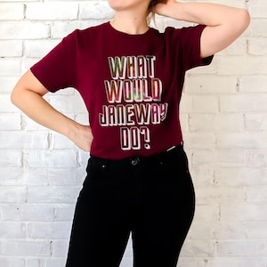 May include: A maroon t-shirt with the text "WHAT WOULD JANEWAY DO?" printed in a colorful, glittery font.