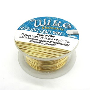 Puede incluir: Una bobina de alambre artesanal de oro de calibre 22, etiquetada como "Dead-Soft Craft Wire" y "Gold/Or/Oro". La bobina tiene 7,3 metros de largo y es resistente al deslustre.