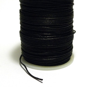 Könnte beinhalten: Eine Spule mit schwarzem gewachstem Kordel, fest gewickelt und bereit für Bastelarbeiten.