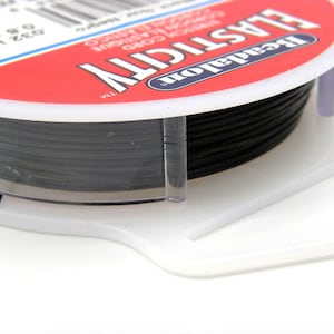May include: A spool of black elastic cord, labeled "Beadalon Elasticity" with a white background and red lettering. The spool is made of clear plastic and has a white label with the text "0.8 mm" and "0.032 in" printed on it.