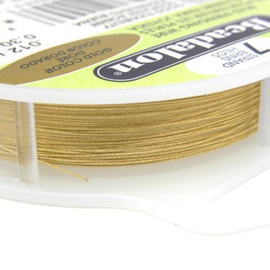 May include: A spool of gold-coloured beadalon beading wire. The spool is labelled "Beadalon" and "7 Strand Soft Beading Wire". The wire is 0.51 mm in diameter.