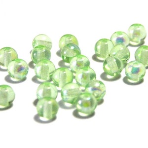 May include: A scattering of translucent, pale green glass beads on a white background. Each bead is spherical with a faceted design, producing a subtle iridescent shimmer. Suitable for jewellery making or craft projects.