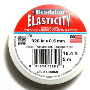 以下が含まれることがあります： 透明なストレッチコードの糸巻き。ラベルには「Beadalon Elasticity Stretch Cord」と記載されており、バーコードと「.020 in 0.5 mm、16.4 ft、5 m、JE0.5T-0005M」のテキストが記載されています。