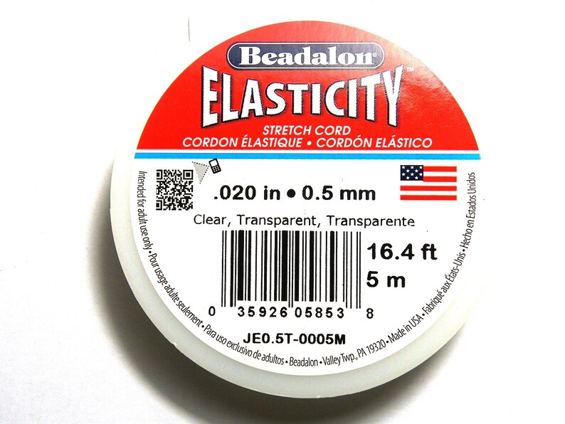 以下が含まれることがあります： 透明なストレッチコードの糸巻き。ラベルには「Beadalon Elasticity Stretch Cord」と記載されており、バーコードと「.020 in 0.5 mm、16.4 ft、5 m、JE0.5T-0005M」のテキストが記載されています。