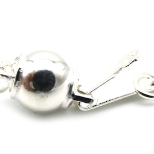 Może przedstawiać: Srebrne zapięcie do biżuterii z okrągłym, pękatym elementem i zawiasową, prostokątną częścią. Zapięcie służy do zabezpieczania element&oacute;w biżuterii, takich jak naszyjniki lub bransoletki, na białym tle.