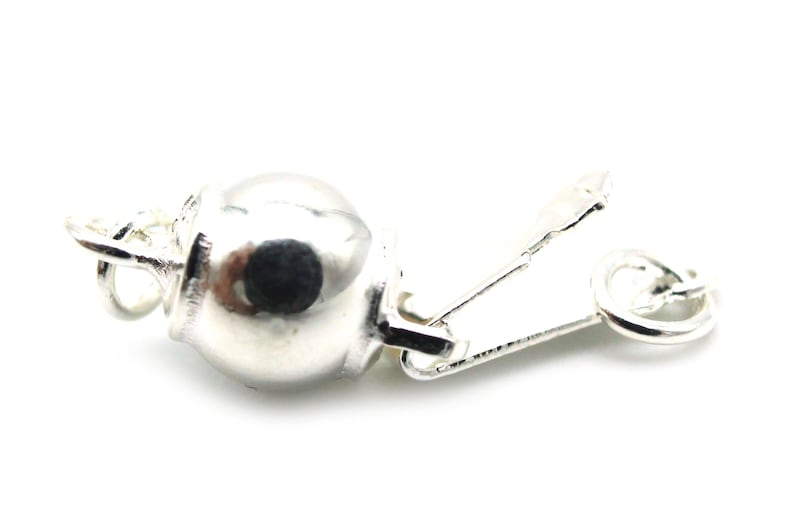 Może przedstawiać: Srebrne zapięcie do biżuterii z okrągłym, pękatym elementem i zawiasową, prostokątną częścią. Zapięcie służy do zabezpieczania element&oacute;w biżuterii, takich jak naszyjniki lub bransoletki, na białym tle.