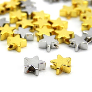 Könnte beinhalten: Eine Streuung von goldenen und silbernen sternförmigen Perlen, perfekt für die Schmuckherstellung oder Bastelprojekte.