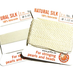 Pode incluir: Dois carretéis de fio de seda natural para enfiar pérolas e contas. Os carretéis são etiquetados com "NATURAL SILK 100% Naturseide" e têm o texto "For stringing pearls and beads" impresso neles. Os carretéis têm 2 metros de comprimento e têm diâmetros de 0,45 mm e 1,02 mm.