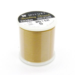 Pode incluir: Uma bobina de fio para miçangas Miyuki de cor dourada, 330dtex, 100% nylon, feita no Japão. A bobina é etiquetada com o nome do produto, o tamanho e o número da cor: WN15R 5.