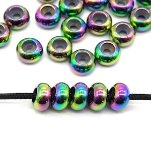 Op de afbeelding: Een close-up van een groep regenboogkleurige, iriserende metalen kralen. De kralen zijn rond met een gat in het midden. Een zwart koord is door vijf van de kralen geregen.