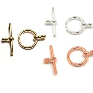 May include: Three sets of gold, silver, and rose gold toggle clasps. Each clasp features a round ring and a straight bar with two round ends.